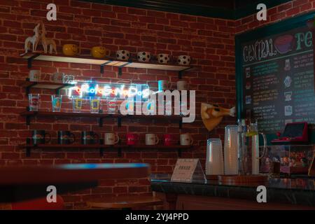 A cozy cafe scene with a brick wall, colorful mugs and glasses displayed on wooden shelves, a neon "Friends" sign, and a menu board Stock Photo