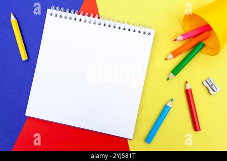 Blank notepad, color pencils and a sharpener on a color paper background. Drawing tools. Kid’s leisure and education materials. Stock Photo