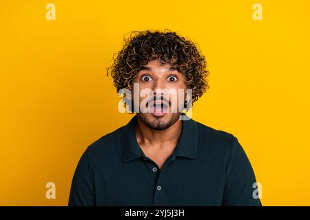 Surprised young man in black shirt against yellow background expressing shock and excitement Stock Photo
