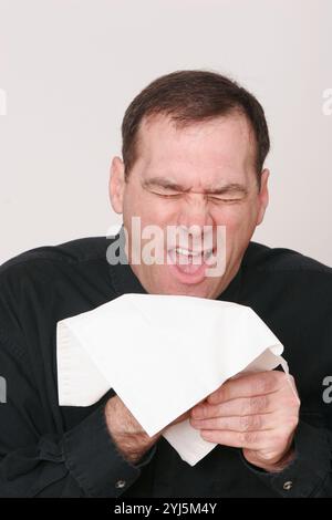 Middle-aged man, with dark hair on white background, makes unusual face, cringing, yelling, sneezing, choking, very expressive, expression Stock Photo