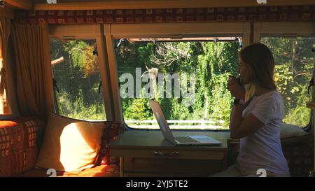 Young woman enjoying cup of coffee while working remotely on laptop Stock Photo