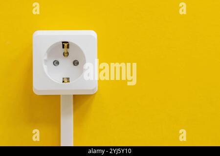 A white electrical outlet is mounted on a vibrant yellow wall. Stock Photo