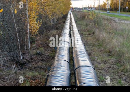 Two insulated pipelines transporting hot water run through an autumn landscape, parallel to a highway Stock Photo