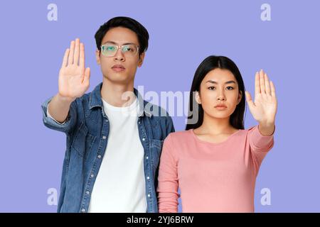 Young asian couple standing over grey studio background, doing stop sign, defense gesture Stock Photo