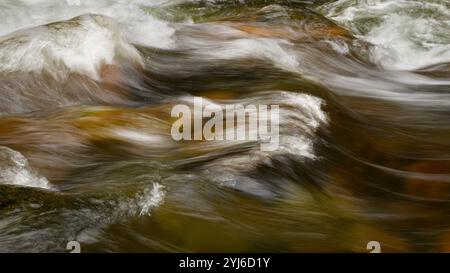 Small wave breaks in mountain stream water over warm tone rocks Stock Photo