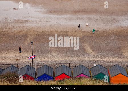 People walk on the beach in front of colourful out of season beach huts at Saltburn Sands, Teesside, England. Stock Photo