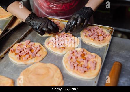 Preparing mini pizzas with diced ham and sauce, perfect for baking in a commercial kitchen Stock Photo