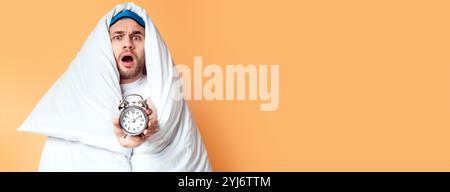 Man overslept concept. Emotional guy in blanket holding an alarm clock Stock Photo