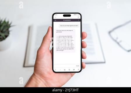Hand holding AI assistant app on smartphone, helping organize daily tasks, improve productivity, and manage time effectively, background shows a works Stock Photo