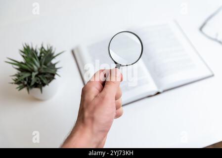 Hand holding magnifying glass over open book, symbolizing keyword search, SEO optimization, and in-depth content analysis, representing focused explor Stock Photo