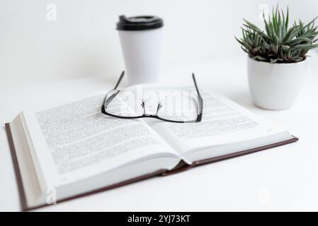 Glasses on open book with coffee cup and plant, symbolizing relaxed reading or study environment, focus on learning, calm ambiance Stock Photo