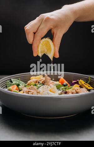 Fresh lemon juice squeezed over a nutritious tuna salad with poached egg, greens and vegetables Stock Photo