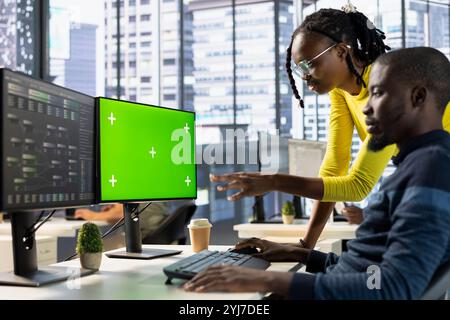 Admin doing software debugging on isolated screen PC, asking for help from coworker, checking errors in lines of code. Worker fixing coding mistakes on chroma key computer, being assisted by colleague Stock Photo
