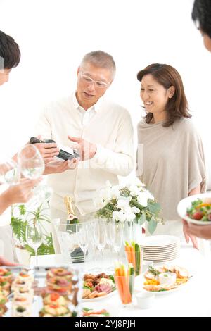 Middle-aged couple and home party guests looking at wine brands Stock Photo