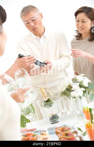 Middle-aged couple and home party guests looking at wine brands Stock Photo