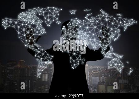 Shadow of a person producing a hologram of a world map with both hands against the backdrop of a city at night Stock Photo