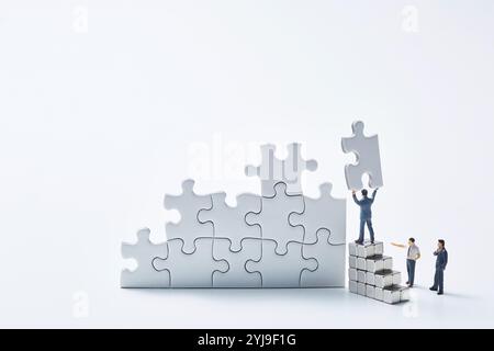 Three miniature dolls assembling a white puzzle Stock Photo