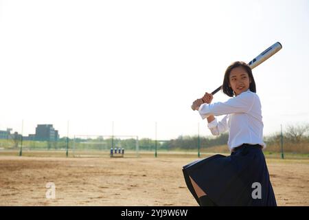 High school girl swinging baseball bat on ground Stock Photo