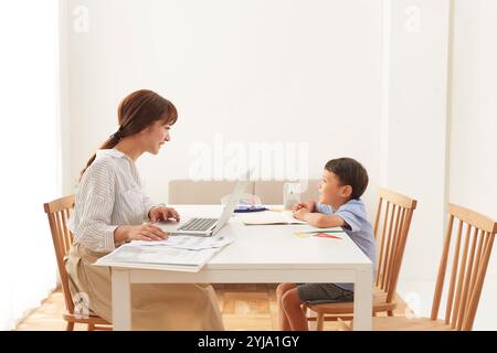 Woman working at home and boy studying at dining table Stock Photo