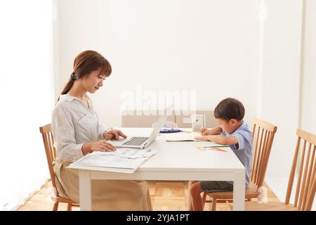 Woman working at home and boy studying at dining table Stock Photo