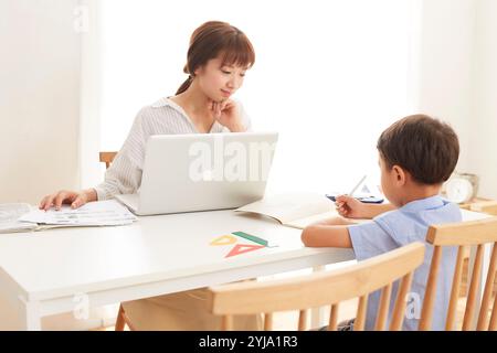 Woman working at home and boy studying at dining table Stock Photo