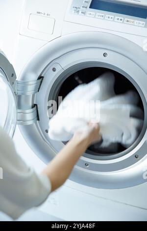 Woman's hand loading laundry into drum washing machine Stock Photo