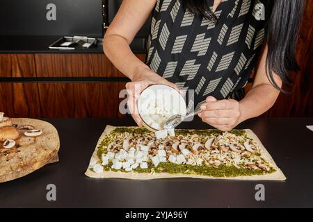 A person adds small cubes of feta cheese to a pesto-covered dough, enhancing flavor and texture in the savory preparation. Stock Photo