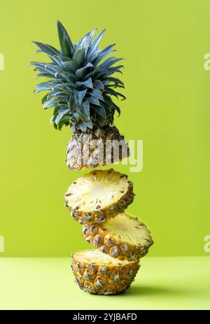 Ripe pineapple levitating in the air. Poster with tropical fruits. Pieces of pineapple on a bright, green background. Stock Photo