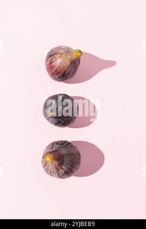 Top view of three ripe figs arranged on a soft pink background, highlighting the figs' natural colors and textures Stock Photo