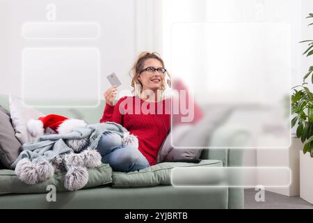 A woman sits comfortably on her couch at home, using her smart glasses to browse the internet for Christmas shopping, while using her credit card to m Stock Photo