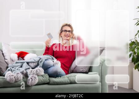 A woman sits comfortably on her couch at home, using her smart glasses to browse the internet for Christmas shopping, while using her credit card to m Stock Photo