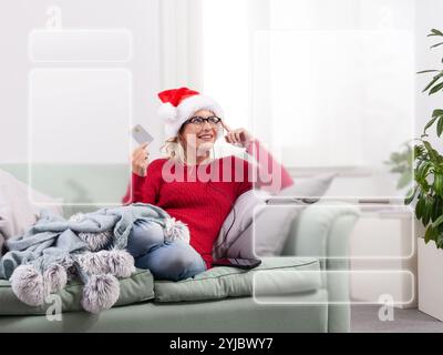 A woman sits comfortably on her couch at home, using her smart glasses to browse the internet for Christmas shopping, while using her credit card to m Stock Photo