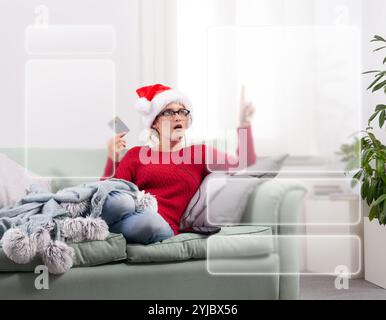 A woman sits comfortably on her couch at home, using her smart glasses to browse the internet for Christmas shopping, while using her credit card to m Stock Photo