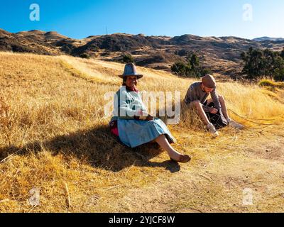 Huaraz, Ancash, Peru - July 22 2024: Quechua Indian Woman is Sitting on the Yellow Grass smiling Next to a Young Man Who is Looking for Something in h Stock Photo