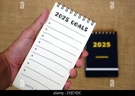 Hand-holding a checklist book for 2025 goals with 2025 calendar. New Year 2025 goals, resolutions, plan, action, checklist concept. New Year's resolut Stock Photo