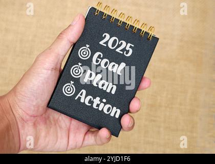 Businessman's hand holding a notebook with writing 2025 goal plan action Stock Photo