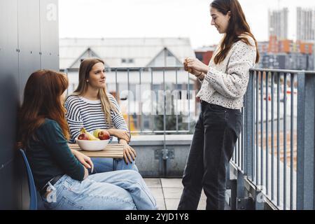 Young caucasian woman college students, sitting on the rood top of their dorm room, eating a snack taking a break from studying, getting some fresh ai Stock Photo