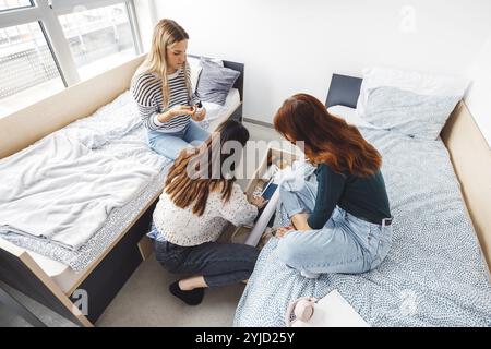 Group of three roommates, college student, young caucasian women, spending time together in their room, studying, talking, having fun, laughing Stock Photo