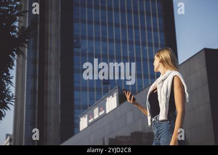 Young caucasian woman in an urban modern setting, skyscrapers in the bacground, using a mobile device. Business woman on a break Stock Photo