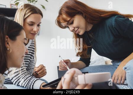 Group of three roommates, college student, young caucasian women, spending time together in their room, studying, talking, having fun, laughing Stock Photo
