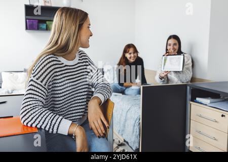 Group of three roommates, college student, young caucasian women, spending time together in their room, studying, talking, having fun, laughing Stock Photo