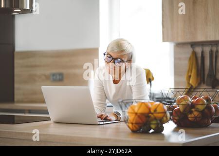 Adult caucasian woman working from home a couple days a week. Adult person working from home, from different rooms in the house, in the kitchen, dinin Stock Photo