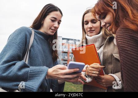 Group of three cheerful female collage students outside their dorm on a cold autumn day, walking on campus to get to their class Stock Photo