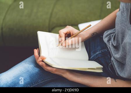 Young caucasian woman with long brown hair in jeans working from home, writing notes. Cheerful woman student studying at home Stock Photo
