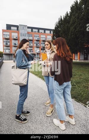 Group of three cheerful female collage students outside their dorm on a cold autumn day, walking on campus to get to their class Stock Photo