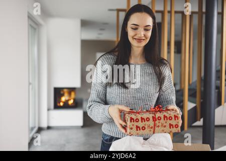 Cheerful young woman excited over a package she just received. Woman getting her christmas gift in the mail. Opening the Christmas present at home Stock Photo