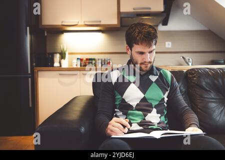 Smiling caucasian man freelancer using laptop studying online working from home, happy casual millennial guy typing on laptop surfing internet looking Stock Photo