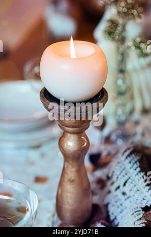Round white candle burning on candlestick on set table for Christmas dinner, creating a warm and festive atmosphere Stock Photo