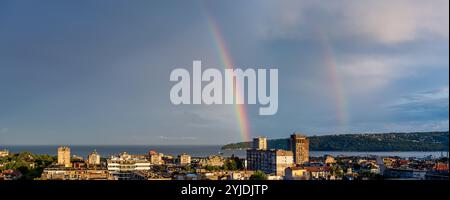 Double rainbow over seaside town at summer evening. Spectacular rainbow over skyline in Varna Bulgaria. Landscape of sity, sky and sea after rain. Stock Photo