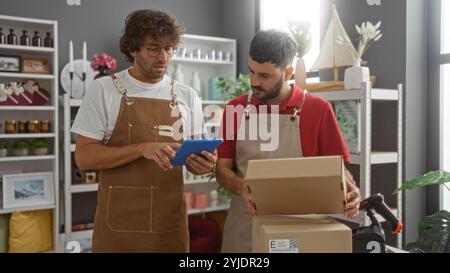 Two men working as shop assistants in a home decor store sorting packages and using a digital tablet in a well-decorated interior Stock Photo